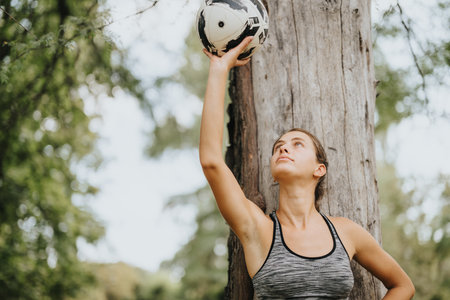 An attractive girl poses with a soccer ball in a sunny park, enjoying physical activity and the natural environment.の写真素材