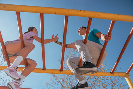Sports couple shaking hands after they made a deal. They are sitting on horizontal metal bars in the...