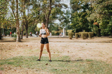 Young woman playing badminton together in a park on a sunny day. She is fit and sporty, enjoying physical activity and the natural environment.の写真素材