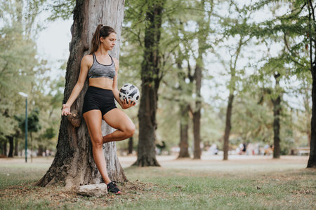 Enjoying a Sunny Day in the Park: Attractive Fit Woman Exercising and Posing with a Footballの写真素材