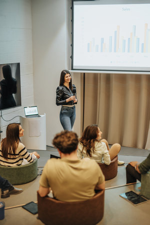 Young, successful businesswoman delivering speech to multiracial business group, discussing charts, profit growth revenue and analyzing statisticsの写真素材