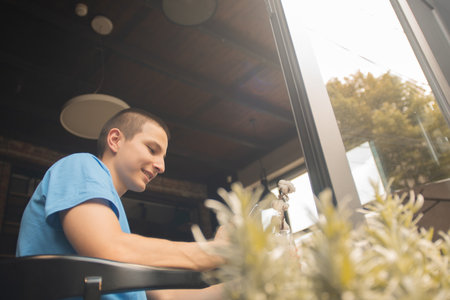 Happy Caucasian Teenager Enjoying Coffee and Browsing Social Media at a Cafe Bar After Schoolの写真素材