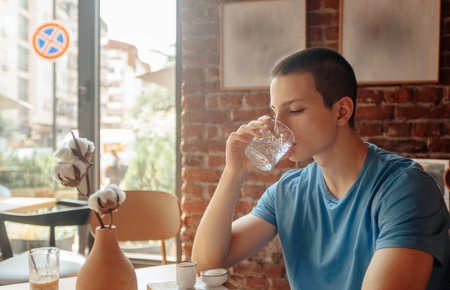 Happy Caucasian Teenager Enjoying Coffee and Networking Indoors on a Sunny Dayの写真素材