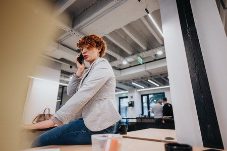 Businesswoman having phone call at the office while sitting on a working desk.の写真素材