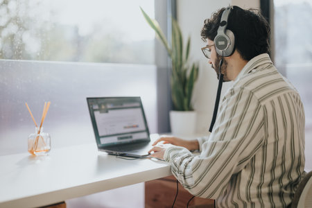 Male business person working on lap top while sitting on a working desk next to the window. Copy...