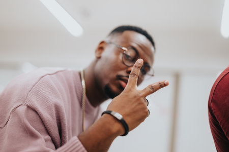 Handsome, black, male employee posing with peace sign to the camera while working with his teammates.の写真素材