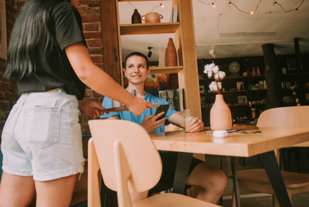 Young Student Enjoying a Sunny Day at a Cafe, Browsing the Internet and Chatting with Friendsの写真素材
