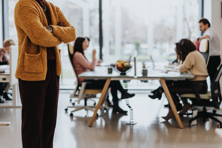 Stylish, unrecognizable, black businessman standing at office. People collaborating at the back gathered at working desk. Cropped photo. Copy space.の写真素材