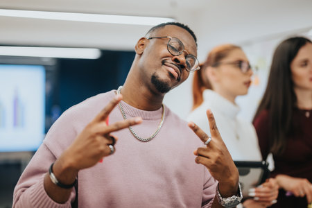 Handsome, black man posing for the camera with peace signs while working with his teammates at the office.の写真素材
