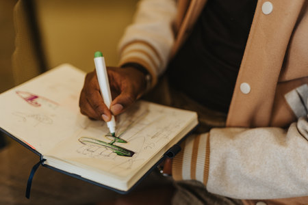 A cropped photo of a male person drawing a sketch in a notebook with a green marker.の写真素材