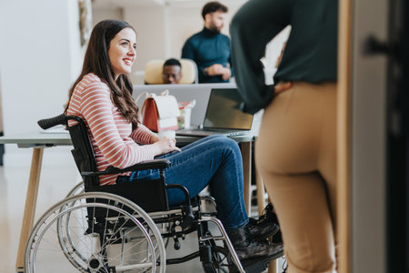 Handicapped female employee in wheelchair collaborating with her colleagues on a project at the office in a pleasant atmosphere.の写真素材