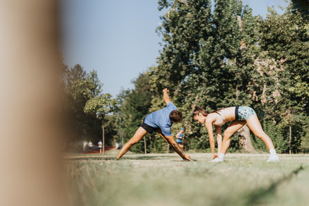 Caucasian couple stretching and warming up in a sunny park. They are motivated, fit, and dedicated to a healthy lifestyle through outdoor exercises.の写真素材