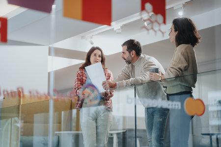 Three professionals engaged in a conversation with reports in hand in a bright office corridor.