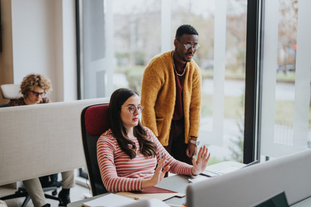 Multiracial team with a female and male colleague discussing work in a well-lit modern office space,...