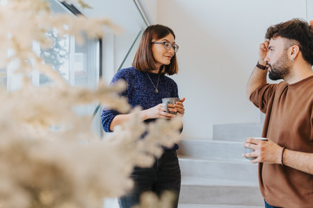 Colleagues engaging in a relaxed conversation during a coffee break in a modern office setting,...