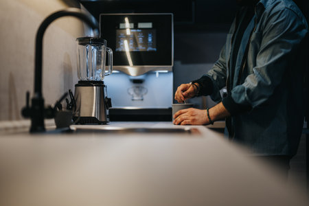 Man preparing beverage at modern kitchen counter with blender and coffee machine.の写真素材