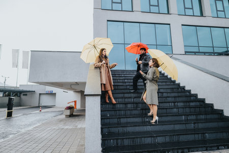 Stylish businesspeople with umbrellas walking down stairs in an urban setting, embodying teamwork and weather preparedness.の写真素材