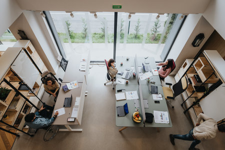 A top view of a bustling modern office space with a diverse team of professionals collaborating at their desks on various projects.の写真素材