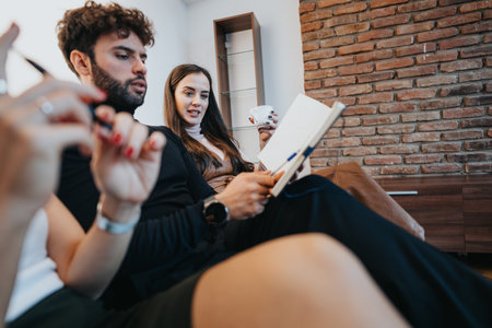 Young couple relaxing at home, woman holding coffee cup while man writes in notebook, casual indoor leisure.の写真素材