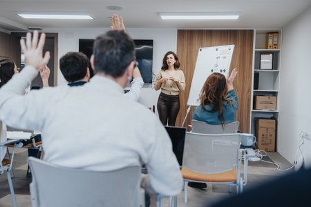 Interactive business training session with engaged employees raising hands. The modern office setting enhances the learning environment.の写真素材