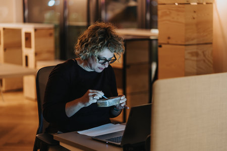 Experienced, businesswoman working late eating takeout at desk in office.の写真素材