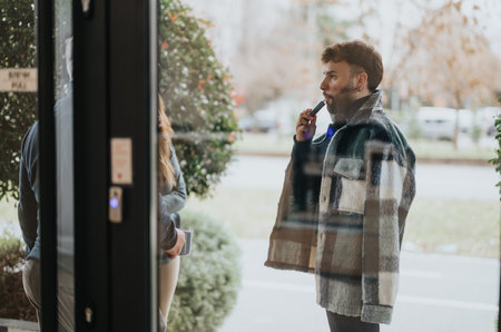 Young man vaping outside modern building through reflective glass windowの写真素材
