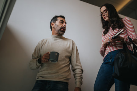 Two employees in a casual setting exchange ideas. A man holding coffee actively listening while a woman checks her phone, preparing for a discussion.の写真素材