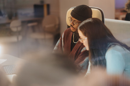 Two professionals collaborating over a laptop in a cozy office setting, engaged in conversation,...