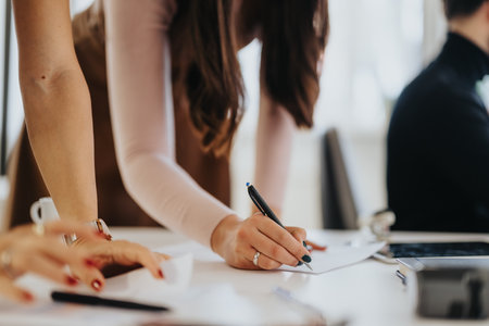 Focused businesswoman writing notes during a collaborative team meeting in a bright modern office.の写真素材