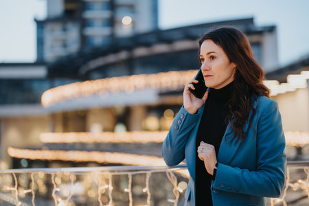 Professional woman in blue blazer talking on phone in urban setting.の写真素材