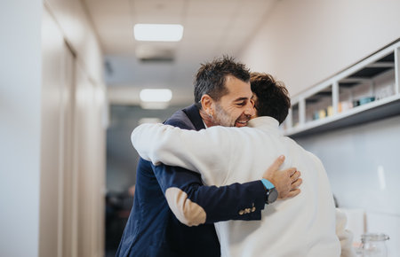 The senior company boss greets his male colleague at work, giving him a hug immediately upon arrival.の写真素材