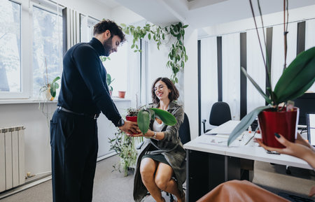 Man giving office plant to smiling female colleague in a modern workspace.の写真素材