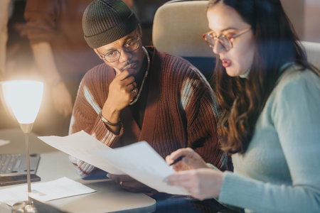 Two business professionals attentively discussing a project, with one holding a smart phone and documents in a well-lit office setting.の写真素材
