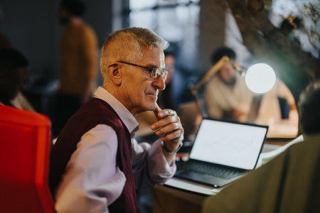 Multigenerational team gathered in office for late evening work discussing strategies for business growth and market expansionの写真素材