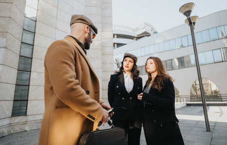 Three young business entrepreneurs engage in an outdoor meeting against a backdrop of city architecture, embodying collaboration and remote working.の写真素材