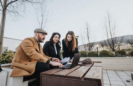 Outdoor business meeting with diverse team working on laptop in public park.の写真素材