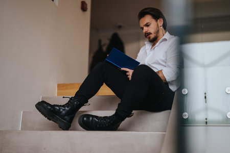 Focused young businessman reading documents on staircase in modern office.