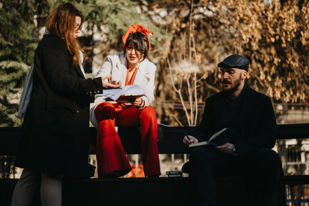 Young business people engaged in a brainstorming session outdoors, strategizing for success amid the city hustle. A diverse trio works harmoniously.の写真素材