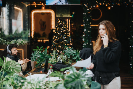 A focused young man with headphones works on his laptop as a woman talks on the phone, with a festive Christmas tree in the background.の写真素材