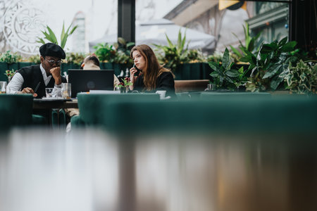 Multiethnic team of business professionals collaborating over a meal in a vibrant, plant-filled restaurant. Concept of teamwork and casual meetings.の写真素材