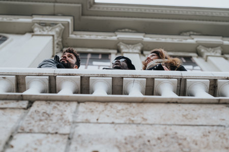A candid shot of three diverse friends gazing into the sky from an ornate balcony, capturing a moment of curiosity and camaraderie.の写真素材