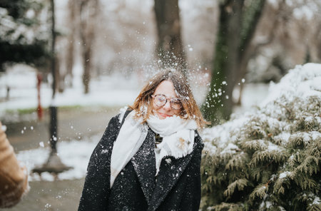 A young businesswoman with glasses is captured outdoors as snow falls gently around her, reflecting a moment of winter joy.の写真素材