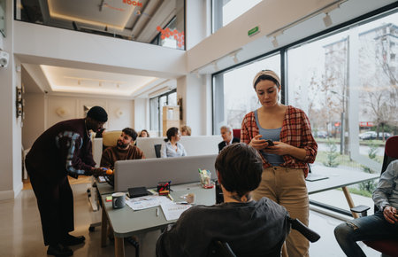 A multi-ethnic group of colleagues interacts in a bright, open-plan workspace, exemplifying teamwork and collaboration.の写真素材