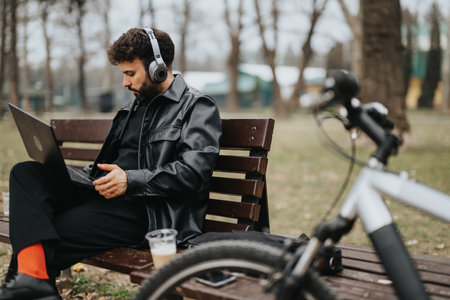 Handsome businessman working on laptop in park with bicycle.