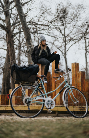 Urban sporty woman using smart phone after cycling in chilly park.