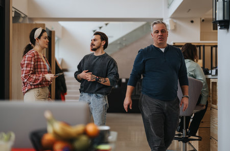 Casually dressed professionals engage in a focused conversation in a modern workplace setting, with a colleague nearby.の写真素材