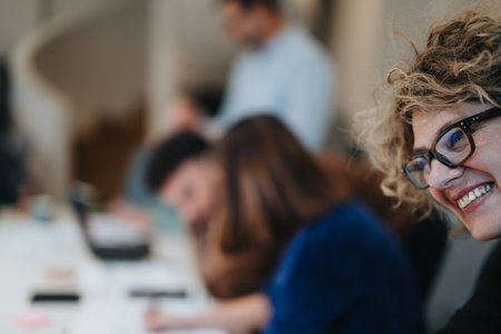Smiling woman in business meeting with colleagues blurred in background.の写真素材