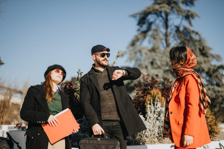 Three multicultural business entrepreneurs engaged in a lively discussion outdoors, bathed in winter sunlight, sharing ideas on a new project.の写真素材
