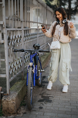 Smiling young woman with headphones using smart phone by her bicycle.
