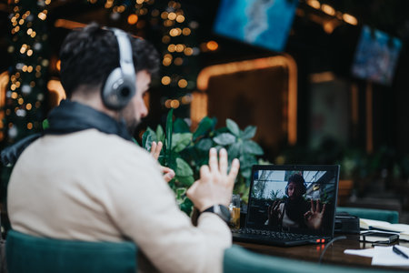 Man in headphones during a remote video conference in a cafe with festive lights.の写真素材